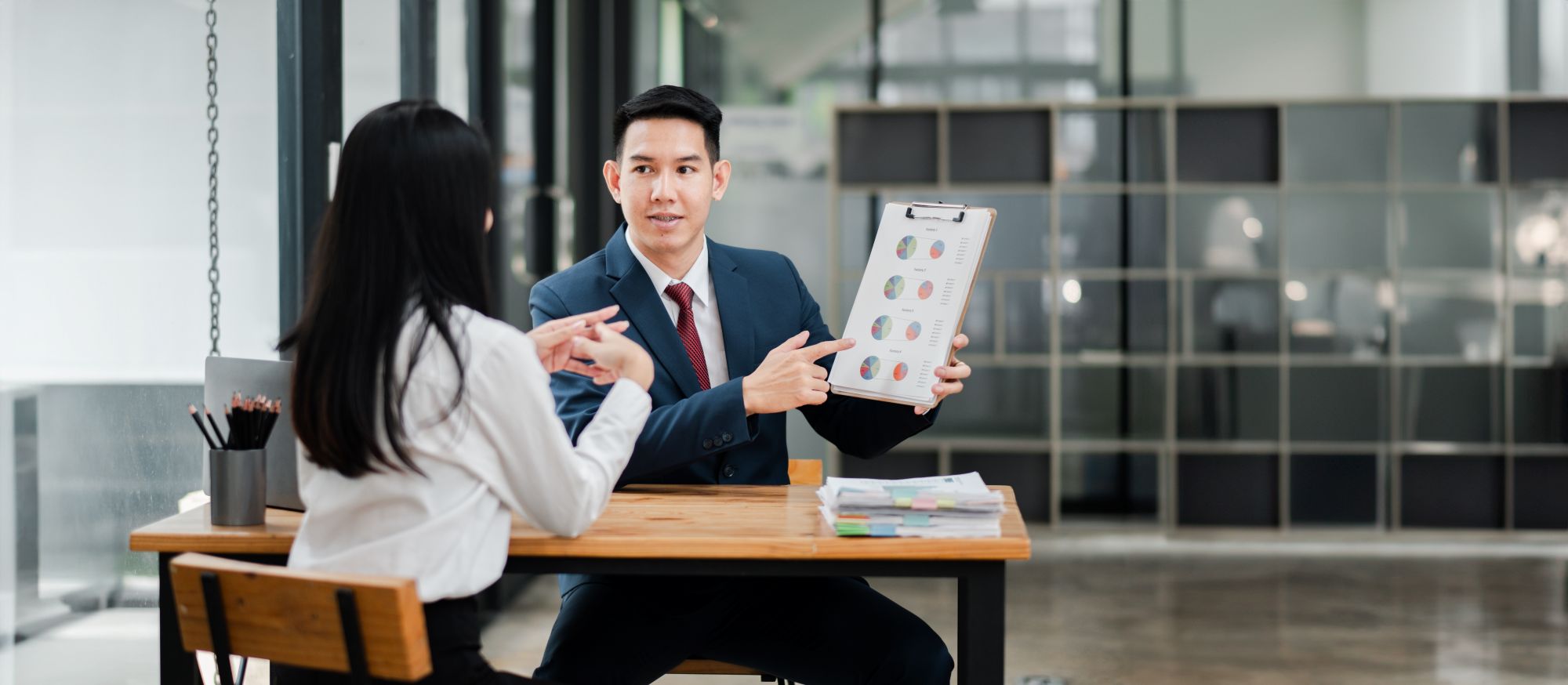 Two Professionals Modern Office Setting Discussing Business Presentation With Charts Graphs