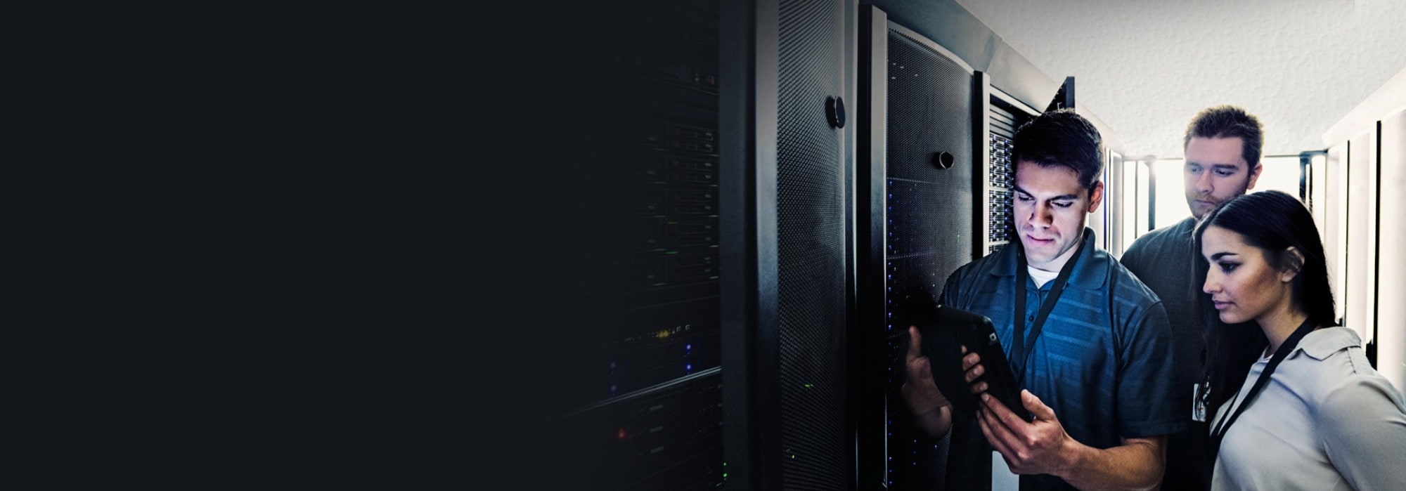 Two males and a female in a tech server room looking at a tablet.